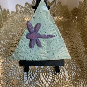 A small triangle shaped sculpture with a purple dragonfly on it.