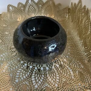 A black bowl sitting on top of a gold doily.