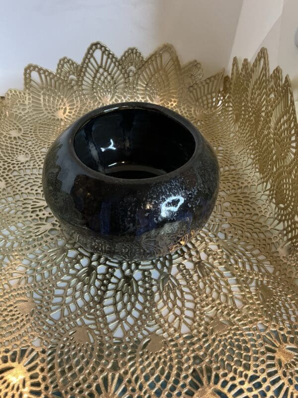 A black bowl sitting on top of a gold doily.