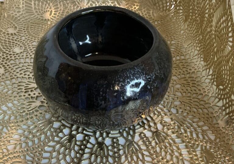 A black bowl sitting on top of a gold doily.